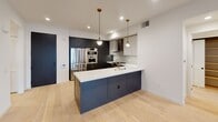 Located at 1333 S Orange Grove Ave in the heart of Los Angeles, CA, this single-floor residence showcases a thoughtfully designed contemporary interior with high-quality finishes throughout. The open-concept kitchen is a true centerpiece, featuring a large island with a white quartz countertop, an integrated wine cooler, and a gold-toned faucet. Dark cabinetry with brushed gold hardware is paired with upper white cabinets and a grey subway tile backsplash, creating a striking two-tone aesthetic. Stainless steel Bosch appliances, including a gas range with a stainless steel hood and built-in wall ovens, complete the chef-quality setup. Pendant lighting with brass accents adds warmth to the space. Light-toned wide-plank hardwood flooring flows seamlessly through the kitchen, living areas, and bedrooms, lending a clean and cohesive look. Bedrooms are bright and airy, featuring recessed lighting and black-framed windows that frame views of the surrounding neighborhood. The bathrooms are finished to a high standard — one features a dual-sink vanity with an illuminated mirror and warm wood cabinetry, while another offers a soaking tub and shower combination with deep blue vertical tile and matte black fixtures. The overall ambiance is modern, refined, and move-in ready.