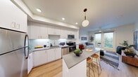 This well-designed one-bedroom, one-bathroom unit at 23040 Military Rd in Kent, WA offers a thoughtful layout that maximizes every square foot of its compact footprint. The open-concept kitchen and living area serves as the heart of the home, where crisp white cabinetry, a subway tile backsplash, and a full suite of stainless steel appliances — including a refrigerator, range, microwave, and dishwasher — create a clean, modern aesthetic. A central island with a gray quartz-style countertop and bar seating adds both functionality and style, illuminated by a globe pendant light. Light wood-tone flooring flows throughout the main living areas, enhancing the bright, airy atmosphere. The living room features large French doors that open to a private balcony, flooding the space with natural light and offering views of the surrounding greenery. The bedroom is a comfortable retreat with a ceiling fan, a broad window framing outdoor views, and access to a closet. The bathroom includes a full tub-shower combination, a white vanity with a gray countertop, and matching wood-tone flooring that ties the space together cohesively. Recessed lighting throughout adds a polished, contemporary finish to this efficient and stylish unit.