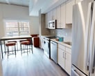 This thoughtfully designed co-living unit offers 1,180 square feet of single-floor living space, accommodating four bedrooms and five bathrooms. The layout is anchored by two fully equipped kitchens, each featuring stainless steel appliances including a range, microwave, dishwasher, and French door refrigerator, complemented by light wood cabinetry, subway tile backsplashes, and clean white countertops. Warm-toned luxury vinyl plank flooring runs throughout the unit, providing a cohesive and durable surface across all rooms. The bedrooms are compact yet functional, with the primary bedroom measuring 240 square feet. Each room features large windows that invite natural light, high ceilings that enhance the sense of space, and private access to bathrooms. The bathrooms are finished in a modern style, with backlit vanity mirrors, white quartz countertops, and wood-toned cabinetry. The primary bathroom includes a double-sink vanity, while others offer single-sink configurations with glass-enclosed showers. A central hallway connects the rooms efficiently, and a dedicated closet provides additional storage. The unit's clean, minimalist aesthetic and practical dual-kitchen layout make it well-suited for shared living arrangements.