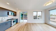 Located at 3725 N 27th St in Tacoma, Washington, this single-floor unit offers a thoughtfully designed, open-concept living space finished with light hardwood flooring throughout. The living and kitchen areas flow seamlessly together, filled with natural light from large windows and a sliding glass door that opens to a landscaped courtyard. The modern kitchen is outfitted with stainless steel appliances — including a gas range, built-in microwave, and dishwasher — complemented by two-toned cabinetry featuring dark upper cabinets and slate-blue lower cabinets, with clean white countertops and a stainless steel sink. The bedroom is generously proportioned, featuring wide windows that frame views of the surrounding Tacoma neighborhood and a closet with sliding doors. A clean, minimal entryway hallway with recessed lighting leads into the main living space. The bathroom includes a dual-sink vanity with a wide mirror, ample drawer storage, and shares space with a convenient stacked in-unit washer and dryer. Recessed lighting and crisp white walls throughout contribute to a bright, contemporary ambiance. The sliding door access to the courtyard adds a welcoming indoor-outdoor connection to the overall layout.
