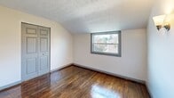 Located at 96 Ledgecrest Ave in New Britain, CT, this two-bedroom, one-bathroom unit offers a practical and efficiently organized layout. Rich, dark hardwood floors run throughout the main living areas and bedrooms, adding warmth and character to the space. Both bedrooms feature textured ceilings and windows that bring in natural light with views of the surrounding neighborhood and greenery. The primary bedroom includes a built-in closet with classic panel bifold doors, while the second bedroom showcases a charming sloped ceiling that adds architectural interest. The kitchen is equipped with warm honey-toned wood cabinetry, a gas range, stainless steel refrigerator, and tile flooring, with a window providing natural light. The bathroom is finished in a clean, all-white palette featuring a tub-shower combo with tiled surround, a window for ventilation and light, a white vanity with sink, and tile flooring. A hallway connects the rooms efficiently, and a staircase provides building access. Wall-mounted sconce lighting accents the hallway area. The unit's neutral walls throughout create a versatile backdrop suitable for a variety of interior styles.