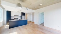 Located at 50 Place De L'Éclipse in Brossard, Quebec, this modern 3-bedroom, 1-bathroom unit offers a well-designed single-floor layout with a clean, contemporary aesthetic throughout. The open-concept kitchen and living area serves as the heart of the home, anchored by a bold navy blue island with a sleek white countertop, complemented by a two-tone cabinet scheme of navy and white. Stainless steel appliances, pendant lighting, and floor-to-ceiling windows fill the space with abundant natural light and frame urban views of the surrounding cityscape. Light hardwood flooring runs throughout the unit, adding warmth against the crisp white walls and exposed concrete ceilings — a distinctive industrial design element present in multiple rooms. Each of the three bedrooms is bright and airy, benefiting from large windows that overlook the developing Brossard skyline and surrounding neighbourhood. Several bedrooms are equipped with built-in sliding closets, offering practical storage solutions. The bathroom features a double-sink vanity with a stone-finish countertop, dark cabinetry, and a large mirror, reflecting a refined and functional design. Overall, the unit presents a cohesive modern style with high-quality finishes and generous natural light throughout.