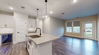 This single-floor unit showcases a contemporary design with a cohesive neutral color palette, wood-look plank flooring, and white five-panel interior doors with matte black hardware throughout. The open-concept kitchen serves as the central hub of the space, featuring white shaker-style cabinetry, quartz countertops, a white subway tile backsplash, and stainless steel appliances including a refrigerator, range, and built-in microwave. A generously sized kitchen island with an undermount sink and pendant lighting above provides additional prep space and seating. In-unit washer and dryer hookups are conveniently located just off the kitchen area.

The living area is bright and open, benefiting from natural light through large windows with roller shades and a glass-paneled exterior door offering outdoor views. Multiple well-proportioned bedrooms feature the same wood-look flooring and neutral walls, providing versatile spaces. Two full bathrooms are included: one with a walk-in glass-door shower and white vanity cabinetry, and another with a soaking tub and shower combination, both finished with matte black fixtures and quartz countertops. Recessed lighting throughout completes the clean, modern aesthetic.