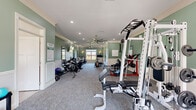 Located at 820 South Gateway Plaza Boulevard in Clarksville, Tennessee, this single-floor community amenity space is thoughtfully divided into two distinct areas designed to support both fitness and recreation. The fitness center is a generously sized, carpet-floored room finished with sage green wainscoted walls, crown molding, and recessed lighting complemented by ceiling fans. It is well-stocked with a wide variety of equipment, including elliptical machines, stationary bikes, a rowing machine, a treadmill, a multi-station cable machine, a power rack, weight benches, and a full dumbbell rack. Wall-mounted mirrors and natural light from multiple windows enhance the open, energizing atmosphere. The adjacent game room offers a vibrant contrast, featuring light hardwood-style flooring, bold two-tone red and white walls, and crown molding. This entertaining space is anchored by a classic billiards table and includes a skee-ball machine and a foosball table, making it ideal for casual social gatherings. Large windows allow natural light to fill the room, while a ceiling fan keeps the space comfortable. Together, these two rooms provide a comprehensive amenity facility that balances active fitness with recreational leisure.