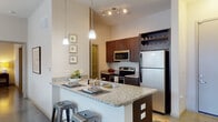 Located at 2000 Front St in Summerville, SC, this well-appointed single-floor residence offers a thoughtfully designed open-concept layout that seamlessly connects the kitchen, dining, and living areas. The kitchen is a standout feature, showcasing rich dark wood cabinetry, granite countertops, a peninsula with bar seating, pendant lighting, and a full suite of stainless steel appliances including a refrigerator, electric range, and microwave. A dedicated laundry and utility area is conveniently accessible from the kitchen corridor. The open living room is bright and airy, benefiting from large windows and glass doors that invite natural light and provide outdoor views. Polished concrete floors extend throughout the main living spaces, lending a clean, contemporary aesthetic, while a ceiling fan adds comfort overhead. The unit features two well-sized bedrooms, each carpeted and filled with natural light from large windows with blinds. Both bathrooms are finished with granite-topped dark wood vanities and polished concrete floors, each equipped with a tub and shower combination. The overall design balances modern finishes with a warm, livable ambiance, making this Summerville residence a refined and functional home.