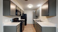 This single-floor unit offers a functional and cohesive layout across its living spaces. The galley-style kitchen is a standout feature, designed with efficiency in mind. Gray cabinetry lines both walls, providing ample upper and lower storage, while light-toned countertops offer generous prep space. Black appliances, including a gas range, over-the-range microwave, refrigerator, and dishwasher, create a bold contrast against the neutral palette. Light wood-look flooring and a textured ceiling complete the kitchen's practical aesthetic.

The living area flows naturally from the entry, where a window allows natural light to brighten the open space. The same wood-look flooring continues throughout, lending visual continuity. Neutral gray walls provide a clean, versatile backdrop throughout the unit.

The bedrooms feature the same consistent flooring and neutral tones. One bedroom includes access to a walk-in closet, offering notable storage capacity, while a ceiling fan adds comfort. Additional bedrooms are well-proportioned with ample wall space.

The bathroom is equipped with a single-sink vanity featuring a light countertop and dark cabinetry, a large mirror, and a full tub-shower combination with a clean white surround. Textured ceilings are consistent throughout the unit, tying the overall design together.