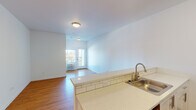Located at 7550 N Lombard Street in Portland's St. Johns neighborhood, Unit 314 is a thoughtfully designed single-floor residence featuring a clean, contemporary aesthetic throughout. The open-concept living and kitchen area serves as the heart of the unit, where warm hardwood-style flooring flows continuously underfoot and crisp white walls create a bright, airy atmosphere. Natural light streams in through a glass-paneled exterior door that opens to a private outdoor space, enhancing the sense of openness in the main living area.

The kitchen is well-appointed with white shaker-style cabinetry, a classic subway tile backsplash, light stone-finish countertops, a breakfast bar peninsula with built-in sink, and stainless steel appliances including a refrigerator and range. A dedicated in-unit laundry closet with a stacked washer and dryer is conveniently accessible just off the kitchen.

The bedroom is a comfortable, well-proportioned room featuring a large sliding window with views of the surrounding neighborhood and a louvered closet door. The bathroom features a full tub-shower combination with a curved curtain rod, a clean white finish, and tile flooring. A louvered utility closet provides additional storage near the main living area. This unit combines practical functionality with modern design in a well-connected Portland location.