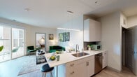 This single-floor residence features a contemporary, open-concept design with a neutral palette of whites and warm beiges throughout. The kitchen is outfitted with light wood cabinetry, a stainless steel sink, dishwasher, and range, complemented by a peninsula with pendant lighting that doubles as a breakfast bar. The kitchen flows directly into the living area, which is bright and welcoming, with wood-look flooring and a sliding glass door that opens onto a private patio offering views of an outdoor pergola structure.

The primary bedroom is a calm, well-lit retreat with multiple windows fitted with horizontal blinds, a ceiling fan, and generous floor space. The second bedroom mirrors this comfortable character, also featuring natural light and a ceiling fan. Two bathrooms serve the residence: one includes a soaking tub with tiled surround and a single vanity, while the second offers a glass-enclosed walk-in shower. Both bathrooms maintain the clean, minimalist aesthetic found throughout the home, with wood-look tile flooring and white fixtures. The overall ambiance is modern, functional, and light-filled.