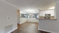Located at 100 Preston Woods Trail in Sandy Springs, Georgia, this two-bedroom, two-bathroom residence offers a thoughtfully designed single-floor layout that balances comfort and functionality. Rich, dark hardwood-style flooring flows throughout the main living areas, creating a warm and cohesive aesthetic. The open living and dining area is bright and airy, with large windows fitted with blinds that invite abundant natural light and views of the surrounding greenery. Crown molding and a textured ceiling add classic architectural detail throughout.

The kitchen features white cabinetry, granite-style countertops, stainless steel appliances including a range and refrigerator, and a breakfast bar that connects seamlessly to the dining and living space. A full-wall mirror in the dining area enhances the sense of openness. Pendant lighting adds a stylish finishing touch overhead.

The bedrooms are generously sized, with plush carpeting providing comfort underfoot and ample natural light. The bathrooms are clean and well-appointed, featuring tiled tub-shower combinations, granite-style vanity countertops, and hardwood-style flooring. A dedicated in-unit laundry room with side-by-side washer and dryer and overhead shelving adds everyday convenience to this well-rounded residence.