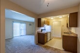 This single-floor residential unit offers a functional and straightforward layout across multiple rooms. The galley-style kitchen is well-appointed with warm wood cabinetry lining both walls, laminate countertops, a double stainless steel sink, and white appliances including a range and refrigerator. Tile flooring in the kitchen transitions to plush carpeting throughout the rest of the unit. A ceiling fan is centrally positioned in the hallway area, connecting the kitchen to the living spaces beyond.

The living room is generously sized, featuring neutral beige walls, soft carpet underfoot, and a large sliding glass door dressed with vertical blinds that allows abundant natural light to pour into the space. A wall-mounted air conditioning unit and baseboard heating provide year-round climate control.

The bedrooms are comfortably proportioned, each carpeted and painted in soft neutral tones. Large windows with blinds invite natural light while baseboard heaters ensure warmth. Closet storage is available within the unit.

The bathroom features a clean white vanity with a built-in sink, medicine cabinet mirrors, and textured walls. Overall, the space presents a practical, comfortable layout with consistent finishes throughout, making it a functional and livable environment.