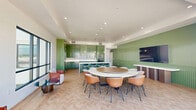 Located at 398 West Valley Boulevard in San Gabriel, California, this single-floor communal space combines a fully equipped kitchen, open dining area, and an impressive rooftop terrace into a cohesive, modern amenity. The interior is anchored by a striking kitchen outfitted with bold sage-green cabinetry that extends floor to ceiling, complemented by white quartz countertops, a marble-tiled backsplash, stainless steel appliances, and a central island with bar seating. Pendant lighting adds warmth overhead, while a herringbone-patterned wood floor runs throughout, lending texture and visual interest to the space. The adjoining dining and lounge area features a round dining table with contemporary leather chairs, a textured green accent wall with a mounted flat-screen display, and recessed lighting set within a coffered ceiling detail. Large sliding glass doors blur the boundary between indoors and out, opening directly onto a spacious rooftop terrace. The terrace is generously appointed with multiple seating arrangements, including rattan sofas, lounge chairs, and dining sets, all set beneath open California skies. Panoramic views of the surrounding San Gabriel Valley neighborhood make this outdoor space a standout feature of the property.
