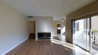 This two-floor home presents a well-connected layout designed for comfortable everyday living. The main living area is anchored by a striking fireplace with a bold black and gold surround, serving as a focal point against a textured accent wall. Warm hardwood-style flooring extends throughout, lending a cohesive and inviting feel to the space. A sliding glass door floods the living room with natural light and provides direct access to the outdoors. The open flow continues into an adjacent dining or secondary living area, enhanced by a ceiling fan and connected to a kitchen featuring warm wood cabinetry. The textured ceiling adds a classic architectural touch, while the neutral wall tones provide a versatile backdrop throughout. A staircase leads to the second floor, offering additional living or sleeping space above. Ample ventilation is provided through ceiling vents distributed across the main level. Overall, the home strikes a balance between practical design and warm, livable character, making it a welcoming space ready to be personalized.