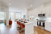 This well-appointed single-floor residence offers a thoughtfully designed open-concept layout that maximizes every square foot. The combined kitchen and living area serves as the heart of the home, bathed in natural light from large windows and a glass balcony door that frames outdoor views. The living room features warm hardwood-style flooring, crisp white walls, and generous ceiling height, creating a bright and welcoming atmosphere.

The kitchen is a standout, outfitted with white shaker cabinetry, a subway tile backsplash, light quartz countertops, and a full suite of stainless steel appliances including a refrigerator, range, and built-in microwave. A central island with bar seating provides additional prep space and a casual dining option. An in-unit stacked washer and dryer are conveniently tucked near the entryway.

The bedroom is a comfortable retreat with a dedicated window offering natural light and outdoor views, ceiling fan, and ample space for furnishings. An adjacent closet provides practical storage. The bathroom features a glass-enclosed walk-in shower with white subway tile, wood-style flooring, and a clean vanity with modern fixtures. Throughout the residence, consistent hardwood-style flooring and a neutral palette create a cohesive, contemporary feel.
