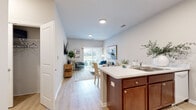 This single-floor residence offers a thoughtfully designed open-concept layout that seamlessly connects the kitchen, dining, and living areas. The kitchen is equipped with rich cherry wood cabinetry, a large peninsula with a double-basin sink and light-toned countertops, a full-size refrigerator, and a range — all set atop durable light wood-style flooring that extends throughout the main living spaces.

The living room is bright and welcoming, featuring large sliding glass doors that flood the space with natural light and provide direct access to a private balcony overlooking a green outdoor area. The bedrooms are carpeted for comfort, with ample natural light from well-placed windows. A versatile secondary room offers flexibility as a home office or additional bedroom.

The bathroom features warm-toned wood cabinetry, a wide vanity with a single-basin sink, a large mirror, and a shower-tub combination with light wood-style flooring. A dedicated in-unit laundry area includes a full-size washer and dryer with overhead shelving for additional storage. Throughout the residence, neutral wall tones, recessed lighting, and clean architectural lines contribute to a modern, comfortable ambiance suitable for everyday living.
