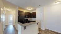 This single-story, 2-bedroom, 2-bathroom residence offers a practical and cohesive layout designed for comfortable everyday living. The open-concept kitchen is a central feature, showcasing dark espresso cabinetry, granite countertops, and black appliances including a refrigerator, electric range, and built-in microwave. A peninsula with an extended granite countertop and bar seating provides a casual dining option while connecting the kitchen to the main living area.

The living room features wood-style plank flooring, a ceiling fan with lighting, and glass French doors that invite natural light and provide outdoor access. The neutral wall tones throughout the unit create a clean, cohesive aesthetic.

Both bedrooms are carpeted and receive natural light through sizable windows with blinds. The primary bedroom includes a ceiling fan, while the second bedroom offers a quiet, functional space. Each bathroom is finished with granite-topped dark vanities and wood-style flooring. One bathroom includes a tub-shower combination, while the second features a more streamlined design. The consistent use of granite and dark cabinetry across the kitchen and both bathrooms ties the unit together with a uniform, polished look.