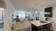This single-floor residence offers a thoughtfully designed open-concept layout that seamlessly connects the kitchen, dining, and living areas. The kitchen is a standout feature, showcasing dark espresso cabinetry, stainless steel appliances, track lighting, and a generous granite-topped island with bar seating — ideal for both meal preparation and casual dining. Wood-style flooring runs throughout the kitchen and main areas, adding warmth and visual continuity.

The living room is bright and welcoming, filled with natural light from large windows dressed with sheer curtains and blinds. Crown molding and a ceiling fan add refined detail to the space. A dedicated dining area sits adjacent, completing the open social zone.

Two well-proportioned bedrooms offer comfortable retreats, each with plush carpeting and ample room for full-sized furniture. The full bathroom features a tub-shower combination, a large mirror, and wood-style flooring, maintaining the clean, neutral aesthetic found throughout the residence.

A dedicated in-unit laundry room houses a full-sized washer and dryer alongside wire shelving for storage — a highly practical inclusion. Overall, the space presents a clean, modern, and functional design with a neutral color palette that creates a calm and cohesive living environment throughout.