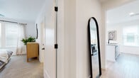 This single-floor residence is designed with a clean, contemporary aesthetic characterized by crisp white walls, light wood-tone flooring throughout the main living areas, and an abundance of natural light streaming through multiple large windows fitted with wood-slat blinds. The open-concept layout connects the kitchen and living areas seamlessly, fostering a cohesive and functional flow.

The kitchen is outfitted with flat-front white cabinetry, quartz countertops, a marble-style tile backsplash, stainless steel appliances, and a built-in range hood. A peninsula island provides casual seating for two, making it equally suited for meal prep and informal dining.

The living area features a private entrance with glass-panel doors and large windows that invite natural light and outdoor views. A well-defined hallway connects the bedrooms, which are carpeted and fitted with ample windows. Each bedroom is generously proportioned, offering comfortable accommodations.

Two bathrooms serve the residence. The primary bathroom features a double-sink vanity with illuminated mirror, wood-look tile flooring, and bright white finishes. The secondary bathroom includes a tiled soaking tub with shower combination and matching contemporary fixtures. A black-framed arched floor mirror accents the hallway, adding a stylish touch to the transitional space.
