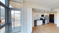 Located at 1810 State Street in San Diego, Unit #401 (Plan F1) is a single-floor residence designed with a clean, contemporary aesthetic. The open-concept layout connects the living area to the kitchen, creating a seamless flow throughout the space.

The kitchen is well-appointed with white shaker-style cabinetry, dark countertops, and a classic white subway tile backsplash. Stainless steel appliances — including a gas range, built-in microwave, and dishwasher — complement the modern design. A deep undermount sink with a sleek faucet adds both style and functionality.

Light-toned hardwood-style flooring runs throughout, lending warmth and continuity to the interior. Recessed lighting provides even illumination across the space. Large floor-to-ceiling windows and a sliding glass door invite generous natural light while offering views of the surrounding San Diego cityscape, enhancing the overall sense of openness.

The unit's neutral color palette of white walls and light flooring creates a bright, airy ambiance well-suited to modern urban living.