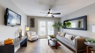 This single-floor residence offers a thoughtfully designed layout that balances comfort and functionality. The living room serves as the heart of the home, featuring wood-look flooring, a textured ceiling with a ceiling fan, and a set of French doors fitted with white blinds that invite natural light and provide access to an outdoor patio area. A tufted gray sofa, glass coffee table, and accent armchair create an inviting seating arrangement, complemented by a large decorative mirror on the wall.

The kitchen is outfitted with gray shaker-style cabinetry, granite-look countertops, a classic subway tile backsplash, and a full suite of stainless steel appliances, including a range, microwave, dishwasher, and refrigerator. Wood-look flooring continues throughout this space, adding visual cohesion.

The bedroom features plush carpet, a bold dark accent wall, and a bright window with sheer curtains that allow ample natural light. The bathroom is finished with a gray vanity, granite-look countertop, a wood-framed mirror, and wood-look flooring. An in-unit laundry closet with a full-size washer and dryer adds everyday convenience. Together, these spaces form a cohesive and well-finished residence.