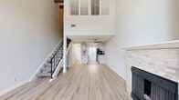 This two-story residence is efficiently designed across two comparable levels, offering one bedroom and two bathrooms. The main level immediately impresses with dramatic double-height ceilings that create a striking sense of vertical space. Light wood-tone flooring runs throughout, complementing the bright, neutral color palette. A stone-clad fireplace anchors one wall of the living area, adding warmth and character, while a staircase with a black metal railing provides a modern design accent. Louvered shutters positioned high on the double-height wall allow light while maintaining privacy.

The galley-style kitchen features granite countertops, cream cabinetry with black hardware, a classic white subway tile backsplash, and stainless steel appliances, including a dishwasher. A window above the counter brings in natural light. A ceiling fan overhead adds functionality to the main living area.

Upstairs, the bedroom showcases exposed painted ceiling beams and soft carpeting underfoot, creating a cozy retreat. A stylish sliding barn door leads to the bathroom, which includes granite countertops, raised-panel cabinetry, and a window for natural light. The upper level also provides additional hallway access to a second bathroom.