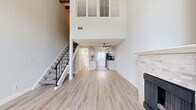 This two-story residence is efficiently designed across two comparable levels, offering one bedroom and two bathrooms. The main level immediately impresses with dramatic double-height ceilings that create a striking sense of vertical space. Light wood-tone flooring runs throughout, complementing the bright, neutral color palette. A stone-clad fireplace anchors one wall of the living area, adding warmth and character, while a staircase with a black metal railing provides a modern design accent. Louvered shutters positioned high on the double-height wall allow light while maintaining privacy.

The galley-style kitchen features granite countertops, cream cabinetry with black hardware, a classic white subway tile backsplash, and stainless steel appliances, including a dishwasher. A window above the counter brings in natural light. A ceiling fan overhead adds functionality to the main living area.

Upstairs, the bedroom showcases exposed painted ceiling beams and soft carpeting underfoot, creating a cozy retreat. A stylish sliding barn door leads to the bathroom, which includes granite countertops, raised-panel cabinetry, and a window for natural light. The upper level also provides additional hallway access to a second bathroom.