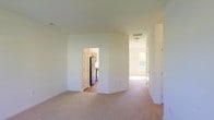 This two-story home at 105 Still Run in Clayton, NJ features a straightforward and functional layout designed for comfortable living. The main level showcases a spacious living area finished with neutral wall-to-wall carpeting, creating a clean and understated atmosphere. Crisp white walls throughout contribute to a bright, open feel, while ceiling vents indicate a central HVAC system for year-round climate control.

A doorway from the main living space leads directly into the kitchen, which features warm wood-toned cabinetry and black appliances, including a full-size refrigerator. The kitchen is finished with hard flooring, providing a practical contrast to the carpeted living areas.

A hallway extending from the living space connects to additional rooms, with natural light visible through a window at the far end, suggesting a bedroom or secondary living area. The corridor provides clear circulation throughout the main level.

The home spans two floors, offering separation between living and sleeping areas. The overall aesthetic is clean and neutral, providing a move-in-ready canvas that lends itself well to personalization.