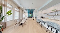 Located at 1520 Alexis Ave in Daytona Beach, FL, this fitness center offers a comprehensive workout environment spread across a single, generously sized floor. The main exercise room is a standout space, featuring striking geometric-patterned carpet in shades of blue, gray, and white that lends a dynamic, modern aesthetic. Ceiling fans and recessed lighting keep the area bright and comfortable, while a row of large windows along the walls floods the space with natural light and views of the surrounding landscape. The main floor is outfitted with an extensive array of equipment, including treadmills, cable machines, a multi-functional power rack, a punching bag, TRX suspension trainers, a plyo box, weight benches, and a full dumbbell rack — catering to cardio, strength, and functional training alike. A mounted flat-screen TV adds convenience for entertainment during workouts. Adjacent to the main floor, a separate studio room provides a quieter setting with light hardwood-style flooring, full-length mirrors, a wall-mounted TV, and equipment such as stationary bikes, a rowing machine, and stability balls — ideal for low-impact or focused training sessions. The hallway connects the two spaces seamlessly, completing this well-appointed, full-service fitness facility.