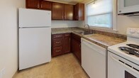 This two-floor residence offers a clean, functional layout with warm hardwood flooring extending throughout the majority of the space. The main level features an open living area anchored by a white-baluster staircase, with a closet conveniently located nearby. The kitchen is well-appointed with rich, dark wood cabinetry, granite-style countertops, a tile floor, and white appliances including a refrigerator, dishwasher, range, and microwave. A window above the sink brings in natural light and outdoor views, enhancing the kitchen's welcoming atmosphere. The staircase, dressed with a patterned runner, connects the two floors and is framed by transom windows above the front entry door, allowing additional light into the stairwell. The upper level hosts generously sized bedrooms with gleaming hardwood floors, neutral walls, and baseboard heating. One bedroom benefits from dual windows that invite natural light and outdoor scenery. The bathroom is finished with white tile, a mosaic accent border, a tub-shower combination, tile flooring, and brushed nickel fixtures, with a window providing ventilation and light. Baseboard heating is present throughout, ensuring comfort across all rooms. The overall ambiance is bright, neutral, and move-in ready.