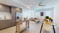This single-floor residence is thoughtfully designed with a clean, contemporary aesthetic that runs consistently throughout each space. Light wood-tone flooring flows seamlessly across all rooms, lending warmth and visual continuity to the open layout.

The kitchen is well-appointed with dark wood flat-front cabinetry extending to the ceiling, stainless steel appliances including a French door refrigerator, range, microwave, and dishwasher, complemented by a classic white subway tile backsplash and light stone countertops. A movable butcher-block island adds flexible workspace and connects easily to the adjacent dining area, which features a glass-top table and access to natural light.

The living room is bright and inviting, with multiple large windows fitted with horizontal blinds that allow generous natural light while maintaining privacy. A ceiling fan anchors the space overhead.

The bedroom continues the bright, airy feel with wrap-around windows on two walls, creating a well-lit and comfortable retreat. The bathroom features a floating vanity with a framed mirror, stone countertop, brushed bronze fixtures, and a full soaking tub with white subway tile surround.

A dedicated laundry room with side-by-side washer and dryer units, along with wire shelving, adds practical utility to the residence.