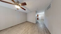 This single-story home presents a cohesive, neutral aesthetic carried consistently throughout its layout. Light wood-look tile flooring runs through the living areas, bedrooms, kitchen, and hallways, creating a unified and easy-to-maintain surface underfoot. The living area is spacious and open, equipped with a ceiling fan and light fixture, and features a large window fitted with horizontal blinds that allows natural light to fill the room.

The kitchen offers warm honey-toned cabinetry, a marble-look countertop, a sink, and a black dishwasher. A back door with a window panel provides additional natural light to the kitchen, which flows into a dedicated dining area illuminated by a modern brushed-nickel chandelier.

The primary bedroom features dual closets side by side, offering generous storage, and is equipped with a ceiling fan. Additional rooms share the same light, neutral palette and wood-look tile flooring.

The bathroom is a well-appointed space featuring large-format wood-look wall tile surrounding the tub and shower combination, accented by a mosaic tile border, complemented by matching floor tile and brushed-nickel fixtures. Throughout, the home maintains a clean, updated appearance with smooth neutral walls and consistent finishes.