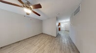 This single-story home presents a cohesive, neutral aesthetic carried consistently throughout its layout. Light wood-look tile flooring runs through the living areas, bedrooms, kitchen, and hallways, creating a unified and easy-to-maintain surface underfoot. The living area is spacious and open, equipped with a ceiling fan and light fixture, and features a large window fitted with horizontal blinds that allows natural light to fill the room.

The kitchen offers warm honey-toned cabinetry, a marble-look countertop, a sink, and a black dishwasher. A back door with a window panel provides additional natural light to the kitchen, which flows into a dedicated dining area illuminated by a modern brushed-nickel chandelier.

The primary bedroom features dual closets side by side, offering generous storage, and is equipped with a ceiling fan. Additional rooms share the same light, neutral palette and wood-look tile flooring.

The bathroom is a well-appointed space featuring large-format wood-look wall tile surrounding the tub and shower combination, accented by a mosaic tile border, complemented by matching floor tile and brushed-nickel fixtures. Throughout, the home maintains a clean, updated appearance with smooth neutral walls and consistent finishes.