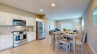 This well-appointed single-floor residence in Canton, Ohio offers a thoughtfully designed open-concept layout that seamlessly connects the kitchen, dining, and living areas. The kitchen is equipped with stainless steel appliances, including a French door refrigerator and range, and features crisp white shaker cabinetry with brushed nickel hardware and granite countertops. Light wood-style flooring flows throughout the main living areas, enhancing the bright and airy atmosphere created by recessed lighting throughout. The dining area comfortably accommodates a full dining set and is open to both the kitchen and living room, making it ideal for entertaining. The living room is bathed in natural light from a large window with exterior views. The entry hallway provides a welcoming transition into the home, complete with a bench and storage. The spacious bedroom features plush carpeting, a ceiling fan, and a large window with vertical blinds. The bathroom is finished with granite-topped vanity cabinetry, wood-look tile flooring, and accessibility-friendly grab bars. A dedicated laundry room houses a full-size Maytag washer and dryer with overhead shelving. The overall ambiance is clean, modern, and move-in ready.