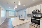 Located at 3400 Nixon Rd in Ann Arbor, Michigan, this well-designed single-floor home offers three bedrooms and three full bathrooms within a thoughtfully arranged floor plan. The open-concept kitchen and living area serves as the heart of the home, featuring a large center island with a built-in sink, crisp white shaker cabinetry, a mosaic tile backsplash, and a full suite of stainless steel appliances including a refrigerator, electric range, and over-the-range microwave. Stylish pendant lighting hangs above the island, adding a modern touch to the space. Wood-look flooring flows throughout the main living areas, while the living room benefits from natural light streaming through sizable windows with blinds and direct access to the outdoors via a glass door. The bedrooms offer a comfortable retreat, with plush carpeting and windows that invite natural light. Three full bathrooms provide ample convenience, each finished with dark-toned vanity cabinetry, white countertops, and wood-look flooring. One bathroom features a tiled tub-shower combination, while another offers a clean, functional layout with a full vanity and mirror. Neutral wall tones and clean lines throughout lend the home a contemporary, move-in-ready aesthetic.