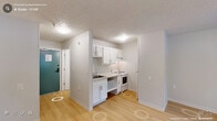 Located at 2504 NC-54 in Durham, North Carolina, this efficiently designed studio unit offers a thoughtfully arranged single-floor layout comprising a living area, kitchenette, and full bathroom. Light wood-style flooring runs throughout the space, lending warmth and visual continuity to every room.

The living area is clean and open, featuring neutral white walls, a textured ceiling, and a wall-mounted HVAC unit positioned beneath a window fitted with horizontal blinds. The window allows natural light to filter in while offering a view of the surrounding greenery.

The kitchenette is neatly outfitted with white shaker-style cabinetry above and below the counter, a stainless steel sink, light stone-pattern countertops, and a white electric range. The layout makes efficient use of the available space, with an open shelving section adding additional storage flexibility. A closet and entry door are accessible directly from the kitchen area.

The bathroom is finished in a clean, all-white palette, featuring a tub-shower combination with grab bar, a toilet, and a single vanity with white cabinetry, a white countertop sink, and a well-lit mirror above. Wood-style flooring continues into the bathroom, maintaining design consistency throughout.

Overall, the unit presents a bright, functional, and well-maintained interior suited for single occupancy.