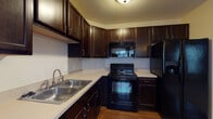 Located at 9220 Worthington Rd in Westerville, Ohio, this single-floor unit offers a well-designed open-concept layout that seamlessly connects the kitchen, dining, and living areas. The kitchen is a standout feature, showcasing rich dark espresso cabinetry extending to the ceiling for ample storage, crisp light countertops, a double-basin stainless steel sink, and a full suite of black appliances including a range, built-in microwave, dishwasher, and refrigerator. A central kitchen island with pendant lighting adds both functionality and visual appeal, anchoring the space between the kitchen and the open living area. Warm hardwood-style flooring flows through the kitchen and dining zone, while plush carpeting covers the spacious living room and bedrooms, creating a comfortable and inviting atmosphere. Multiple windows throughout allow for generous natural light, offering views of the surrounding exterior. The bedrooms are well-proportioned and include access to closet space. The bathroom features dark vanity cabinetry consistent with the kitchen's design language, a framed mirror, light countertops, and tile flooring, maintaining a cohesive aesthetic throughout the unit.