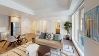 Located at 555 N Spring St in the heart of downtown Los Angeles, this contemporary two-story residence offers a thoughtfully designed layout with modern finishes throughout. The main living area features large floor-to-ceiling windows that flood the space with natural light and provide views of the surrounding urban streetscape. A tray ceiling adds architectural dimension to the living room, which is anchored by warm hardwood-style flooring and an open, airy ambiance. The kitchen is well-appointed with light wood cabinetry extending to the ceiling, white quartz countertops, a classic subway tile backsplash, and a full suite of stainless steel appliances including a range, microwave, dishwasher, and refrigerator. The bedroom is a calm retreat with access to a private outdoor area through a sliding glass door, bringing in soft natural light. The bathroom features a clean, minimalist aesthetic with a wood-toned vanity, white quartz countertop, mirrored medicine cabinet with open shelving, and tiled flooring. A staircase connects the two levels, visible in the architectural overview of the space. Throughout, the design maintains a consistent palette of soft whites, warm wood tones, and neutral accents, creating a cohesive and modern urban living environment.