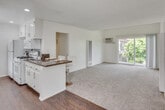 Located at 7051 Maddox Dr in Huntington Beach, California, this single-floor residence offers a thoughtfully laid-out living space with a blend of functional design and comfortable finishes throughout. The kitchen is a standout feature, appointed with crisp white cabinetry, rich dark granite countertops, hardwood flooring, and white appliances including a gas range, refrigerator, and built-in microwave. A breakfast bar with modern bar stools provides a casual dining option and connects seamlessly to the open living area. The living room is generously sized, featuring soft wall-to-wall carpeting, a vaulted ceiling with exposed wooden beams, and sliding glass doors that open to a private balcony, filling the space with natural light and outdoor access. The bedrooms are well-proportioned, each with plush carpeting and large windows dressed with vertical blinds, allowing ample natural light. One bedroom showcases the same distinctive vaulted beam ceiling detail. The bathroom is tastefully updated with dark granite countertops, a framed vanity mirror, white cabinetry, and a glass-enclosed shower. Throughout the residence, neutral tones and clean lines create a calm, welcoming ambiance well-suited to the Southern California lifestyle.