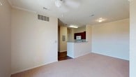 This single-floor residence offers a practical and comfortable layout designed for everyday living. The open living area is finished with plush wall-to-wall carpeting and features a ceiling fan, creating a relaxed and airy atmosphere. A sliding glass door leads to an outdoor balcony, allowing natural light to fill the space. The kitchen is positioned adjacent to the living area and is defined by a raised peninsula counter that serves as a natural divider. Rich, dark wood cabinetry lines the kitchen walls, complemented by light countertops, a coil-burner electric range, and an over-the-range microwave. The bedrooms are generously sized, each equipped with ceiling fans, carpeted floors, and windows fitted with blinds that provide both natural light and privacy. Closet access is available within the bedrooms for ample storage. The bathrooms feature wood-look hard flooring, offering a clean contrast to the carpeted areas. One bathroom includes a tiled soaking tub and shower combination, a toilet, and an overhead storage cabinet, while another features a vanity with a large mirror and multi-drawer cabinetry. Throughout the unit, neutral warm-beige walls and clean white trim create a cohesive, understated aesthetic.