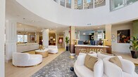 Located at 601 W Bacon St in Richmond, VA, The James presents a thoughtfully designed, single-floor community facility that blends elegance with functionality. The centerpiece of the space is a striking cylindrical rotunda entry, distinguished by soaring double-height ceilings, floor-to-ceiling windows that flood the area with natural light, and polished grey marble flooring. Curved white sofas with gold accents complement a sleek reception desk branded with "The James," creating a welcoming first impression.

Beyond the entry, the space opens into generous lounge areas finished with light hardwood flooring, mid-century modern furnishings, sculptural brass chandeliers, and curated artwork. These seating areas are arranged to encourage both social interaction and relaxed conversation, with ample natural light streaming in through large windows.

A dedicated café-style lounge features a warm gold ceiling, bold pendant lighting, a patterned tile backsplash, a service counter, and bistro-height seating with rich green velvet chairs — ideal for casual gatherings or refreshments.

A private conference room rounds out the facility, offering an intimate setting with a round wood table, leather task chairs, an accent wall in muted sage green, and a stylish overhead fixture. Together, these spaces reflect a refined, contemporary aesthetic tailored for community engagement and leasing activities.