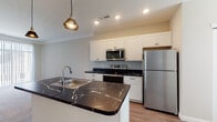 Located at 7325 Liberty Summit Dr in Powell, Ohio, this single-floor home offers a thoughtfully designed layout with modern finishes throughout. The kitchen serves as a central highlight, featuring striking dark marble countertops with gold veining, crisp white shaker-style cabinetry, and a full suite of stainless steel appliances including a refrigerator, range, and built-in microwave. A central island with an integrated sink and stylish pendant lighting above adds both functionality and visual appeal, seamlessly connecting the kitchen to the open living area. The living space is generously sized, finished with plush neutral carpet and large sliding glass doors dressed with vertical blinds that invite natural light and provide outdoor access. Crown molding adds a refined architectural touch to the main living area. The bedrooms continue the neutral, comfortable aesthetic with soft carpet flooring, ceiling fans, and windows fitted with blinds for natural light and privacy. The bathroom is well-equipped with white cabinetry, dark marble countertops consistent with the kitchen's design language, a large mirror with vanity lighting, and durable wood-look vinyl flooring. Throughout the home, a cohesive neutral color palette and quality finishes create a clean, move-in-ready atmosphere.