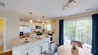 This well-designed multi-story home spans three floors, offering a thoughtfully laid out living experience across each level. The kitchen serves as a centerpiece of the main living area, boasting white shaker-style cabinetry, granite countertops, a classic subway tile backsplash, and a full suite of stainless steel appliances including a side-by-side refrigerator, electric range, microwave, and dishwasher. A large island with bar seating provides additional workspace and casual dining. Pendant lighting and track lighting illuminate the space, which opens directly to a dining area and sliding glass doors leading to an outdoor patio with lush greenery views. The living room features vaulted ceilings and ample natural light from multiple windows, creating an open and airy atmosphere. The bedrooms are carpeted and generously sized, with windows overlooking wooded surroundings. The primary bedroom includes an en-suite bathroom equipped with a glass-enclosed shower. A secondary full bathroom features granite countertops, a large vanity mirror, and a tub-shower combination. Additional bedrooms offer comfortable accommodations with natural light. The home's neutral color palette and clean finishes provide a cohesive, move-in-ready aesthetic throughout all three floors.