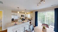 This well-designed multi-story home spans three floors, offering a thoughtfully laid out living experience across each level. The kitchen serves as a centerpiece of the main living area, boasting white shaker-style cabinetry, granite countertops, a classic subway tile backsplash, and a full suite of stainless steel appliances including a side-by-side refrigerator, electric range, microwave, and dishwasher. A large island with bar seating provides additional workspace and casual dining. Pendant lighting and track lighting illuminate the space, which opens directly to a dining area and sliding glass doors leading to an outdoor patio with lush greenery views. The living room features vaulted ceilings and ample natural light from multiple windows, creating an open and airy atmosphere. The bedrooms are carpeted and generously sized, with windows overlooking wooded surroundings. The primary bedroom includes an en-suite bathroom equipped with a glass-enclosed shower. A secondary full bathroom features granite countertops, a large vanity mirror, and a tub-shower combination. Additional bedrooms offer comfortable accommodations with natural light. The home's neutral color palette and clean finishes provide a cohesive, move-in-ready aesthetic throughout all three floors.