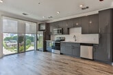 Located steps from Centennial Olympic Park in the heart of Atlanta, this contemporary single-floor residence offers a thoughtfully designed layout with modern finishes throughout. Warm hardwood-style flooring flows seamlessly across every room, lending a cohesive and inviting feel to the entire space.

The open-concept kitchen is a standout feature, outfitted with sleek two-tone cabinetry in charcoal and steel blue, white quartz countertops, a clean tile backsplash, and a full suite of stainless steel appliances including a range, microwave, dishwasher, and refrigerator. A large sliding glass door floods the kitchen and living area with abundant natural light and provides direct access to an outdoor view of the surrounding neighborhood.

The hallway connects the living spaces to a well-appointed bathroom, which features a glass-enclosed walk-in shower with white tile surround, a dark-finish vanity with a white countertop, and wood-look flooring that continues the home's design language. A separate bedroom offers a clean, bright retreat with recessed lighting and convenient access to an in-unit stacked washer and dryer tucked neatly behind louvered closet doors. The corridor also features stylish paneled gray doors, adding a modern architectural touch to the home's interior.