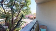 This single-floor space includes a private balcony that serves as a notable feature, offering an elevated outdoor vantage point with views of lush, mature trees and a bustling streetscape below. The balcony is finished with a textured stucco exterior wall and a smooth railing, providing a functional and relaxed setting for outdoor enjoyment. From this perch, the surrounding neighborhood is visible, including nearby commercial establishments framed by generous tree canopy, giving the space a pleasant connection to its urban environment. The interior areas of the space were not well-illuminated in the available imagery, limiting a full assessment of the rooms; however, glimpses suggest standard residential layout elements including doorways and enclosed rooms. The overall character of the space is shaped largely by its exterior-facing balcony, which provides natural light and an open-air atmosphere. The textured building facade and elevated position above street level contribute to a sense of privacy while maintaining visual engagement with the surrounding area. This space appears well-suited for those who value an outdoor connection within an urban residential setting.