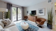 This single-floor residence is thoughtfully designed with a contemporary aesthetic, combining clean lines, light wood-look flooring, and a neutral color palette throughout. The open-plan kitchen is a functional centerpiece, equipped with stainless steel appliances, wood-grain cabinetry, a white subway tile backsplash, and light quartz countertops extending to a breakfast bar island — providing both prep space and casual seating.

The living area is bright and welcoming, featuring sliding glass doors that open to a private balcony with tropical outdoor views, allowing ample natural light to fill the space. Two well-proportioned bedrooms each offer a calm retreat; the primary bedroom includes a walk-in closet and large windows, while the secondary bedroom benefits from natural light and a serene, neutral decor.

Both bathrooms are finished with the same wood-look tile flooring and dark wood-grain vanity cabinetry. The primary bathroom features a glass-enclosed walk-in shower with clean tile surrounds and a tall storage cabinet, while the secondary bathroom offers a full soaking tub with shower combination. Together, the rooms reflect a cohesive, modern coastal design sensibility throughout.