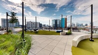 Located at 645 Division St in Nashville's vibrant Gulch neighborhood, this rooftop terrace offers a well-appointed outdoor amenity space with striking views of the downtown Nashville skyline. The terrace is defined by a contemporary architectural aesthetic, with the surrounding building clad in sleek vertical metal panels and expansive floor-to-ceiling curtain-wall glazing that reflects the cityscape and open sky.

The outdoor space is thoughtfully designed for both recreation and relaxation. A putting green with multiple holes provides a unique recreational feature, bordered by clean concrete seating walls and open sightlines to the city beyond. String lights strung between tall poles add an ambient element suitable for evening gatherings.

Generous planted beds and green roof areas introduce natural texture throughout, featuring ornamental grasses, flowering perennials, and low-growing groundcovers. Comfortable lounge seating and chaise lounges are positioned to take full advantage of the panoramic urban views, while raised planters filled with seasonal blooms and grasses add color and vibrancy.

A covered passageway with a warm wood-paneled ceiling connects different sections of the terrace, providing shade and shelter. Large-format pavers create clean, durable walkways throughout. The overall ambiance is modern and urban yet welcoming, balancing active amenities with serene green spaces high above the Nashville streetscape.
