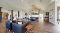 Located at 277 Bend Blvd in Westerville, Ohio, this single-story community clubhouse blends modern design with warm, inviting finishes throughout. The entry foyer welcomes visitors with a striking herringbone hardwood floor pattern and large glass double doors that flood the space with natural light. The expansive main gathering area is anchored by soaring vaulted ceilings, a ceiling fan, and an open-concept layout with wide-plank hardwood flooring that flows seamlessly throughout. This central hub accommodates multiple seating arrangements, making it ideal for both large and small gatherings. A fully equipped kitchen area features rich walnut cabinetry, stone countertops, stainless steel appliances, and a dishwasher, providing ample functionality for events and everyday use. A sophisticated lounge room showcases a dramatic floor-to-ceiling stacked stone fireplace, a wood-paneled ceiling, and expansive windows that bring in views of the outdoors. A dedicated media lounge with deep charcoal walls and plush, tiered seating offers a cozy retreat. The conference room, named "Timbers," provides a functional workspace with a reclaimed wood table, upholstered seating, and a whiteboard. Additional areas include a flexible open hall and wall-mounted display spaces, completing this well-appointed community facility.
