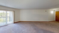 Located at 9851 Harrison Rd in Bloomington, Minnesota, this single-floor residence offers a practical and comfortable layout designed for everyday living. The kitchen is efficiently arranged with warm honey-toned cabinetry, light countertops, and white appliances including an electric range, over-the-range microwave, and refrigerator. Light tile flooring runs throughout the kitchen, while a pass-through window connects it to the adjacent living area, enhancing the open feel between spaces. The living room is generously sized, featuring soft carpeting, neutral walls, and a ceiling fan that adds both function and a focal point to the room. Natural light filters in through vertical-blind-covered windows, creating a bright and welcoming atmosphere. The bedrooms are carpeted and offer ample storage with mirrored sliding closet doors that reflect light and add a sense of depth to the rooms. The full bathroom is clean and straightforward, featuring a single-sink vanity with warm wood cabinetry, a wide mirror, tile flooring, and a shower-tub combination. Throughout the residence, consistent warm wood trim, textured ceilings, and neutral tones contribute to a cohesive and livable aesthetic.