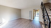 This two-story residence in Suisun City, California is designed with a practical, functional layout spread across two levels. The main floor features wood-style laminate flooring throughout, lending a clean, cohesive look to the living areas. A wall-mounted heating unit is positioned in the main living space, which opens toward a hallway leading to a sliding glass door that brings in natural light and outdoor views. A carpeted staircase with a sleek metal railing connects the two floors, with a wall-unit air conditioner conveniently located near the entry.

The kitchen is anchored by a peninsula with granite-style countertops and a built-in sink, offering an open connection to the living area. White cabinetry lines the walls, complemented by stainless steel appliances including a gas range and refrigerator. Louvered cabinet doors add a subtle textural detail.

Upstairs, the bedrooms are carpeted and finished with neutral tones, each featuring windows that admit natural light and outdoor views of surrounding greenery. The bathroom is well-appointed with wood-look tile flooring, a white vanity with granite-style countertop, and a full tub-shower combination, completing the home's straightforward and well-maintained interior.