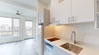Located at 5460 N Interstate Ave in Portland, Oregon, this one-bedroom, one-bathroom unit offers a thoughtfully designed layout that maximizes every square foot. The interior is finished in a clean, modern aesthetic throughout, with light wood-tone flooring and crisp white walls that create a bright, cohesive feel across all rooms.

The bedroom is the largest room in the unit, benefiting from a generous picture window that frames outdoor views and fills the space with natural light. A ceiling fan adds comfort and functionality to the room.

The kitchen is efficiently designed with white cabinetry, open shelving, and white quartz countertops. It is equipped with a stainless steel sink with a pull-down faucet, an electric cooktop, a built-in microwave, and a full-size refrigerator. Under-cabinet lighting provides practical task illumination. A glass door at the end of the kitchen leads to a private balcony, enhancing the sense of openness.

The bathroom features the same light wood-tone flooring found throughout the unit, a white vanity with modern hardware, and a separate shower and toilet area. A hallway connects the rooms and provides additional storage potential.

The overall ambiance of the unit is clean, minimalist, and move-in ready, well-suited for those seeking a streamlined living space in North Portland.